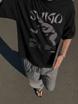 Remera marrón oversize con efecto acid wash, corte amplio y mangas cortas. Presenta un estampado frontal en tonos celestes y grises con la inscripción 'Sumo', una ilustración de un luchador de sumo y detalles tipográficos alusivos a un álbum musical.