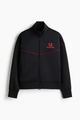 Campera deportiva de efecto neopreno color negro, con cuello alto, cierre frontal bidireccional y bolsillos laterales. Presenta detalles de ribetes rojos en el pecho y el logo de Honda bordado en rojo.