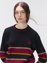 Sweater clásico de punto cable con cuello redondo a la base, mangas largas y fit al cuerpo. De color marrón con franjas horizontales violetas y amarillas, cuenta con el cuello, puños y ruedo acanalados, además de un pequeño logo bordado en el pecho.