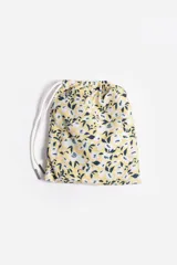 Short de baño celeste con estampado de hojas pequeñas en tonos verdes y blancos. Cuenta con cintura elástica con cordón ajustable, bolsillos laterales y un parche circular con logo en la parte inferior.