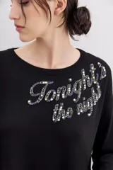 Sweater negro de manga larga y calce holgado, con terminaciones en punto rib. Presenta un bordado frontal con la frase "Tonight the night" realizado con canutillos y piedras de colores.