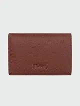 Billetera compacta Longchamp modelo Le Foulonné, confeccionada en cuero granulado color marrón, con logo de la marca grabado en el frente.