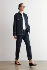 Camisa de jean de corte recto y calce holgado, con cuello clásico, cierre frontal con botones metálicos y dos bolsillos delanteros con solapa y botón.