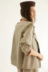 Chaqueta corta de inspiración motoquera color beige, confeccionada en lino fantasía, sin forro, con cierres decorativos, broches de presión y bolsillos delanteros funcionales. Presenta detalle bajo el cuello y en vueltas de mangas en color mostaza y rayas.
