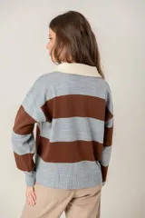 Buzo de tejido de punto con diseño de rayas horizontales anchas en color gris y marrón. Presenta cuello polo en tono crema con cierre frontal de dos botones y mangas largas con puños acanalados.