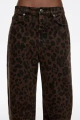 Pantalón de corte barrel color negro, con tiro medio, cierre frontal con botón y cremallera, cinco bolsillos y detalle de tachas metálicas a lo largo de las costuras laterales.