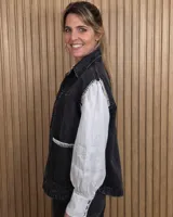 Chaleco de denim color marrón, confeccionado en 100% algodón, con bolsillos frontales amplios, cierre de botones y costuras decorativas bordadas en blanco en los bordes y los bolsillos.