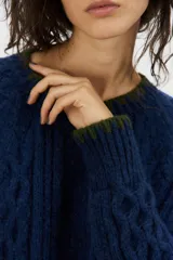 Sweater de punto de mohair color beige, con cuello redondo, mangas largas y detalles de terminación en color negro en el cuello, puños y ruedo.