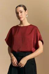 Top negro de manga corta con silueta amplia y caída fluida, confeccionado en un tejido liviano con leve brillo. Presenta un botón de nácar en la espalda con una pequeña abertura y mangas amplias tipo kimono.