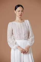 Blusa de encaje blanco con diseño floral geométrico, cuello redondo y mangas largas abullonadas con puños ajustados.