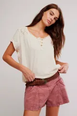 Remera henley de algodón liviano y jaspeado, de calce relajado, color blanco off-white, con mangas cortas, botonadura al cuello, aplicaciones de encaje y ruedo enrollado.