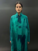 Tapado largo de lana merino color verde con teñido tie-dye en tonos oscuros. Tiene corte particular en los hombros y bolsillos laterales.