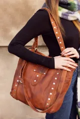Bolso tipo tote bag de cuero negro con apliques metálicos plateados.