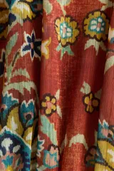 Vestido túnica corto y oversized de tejido plano con estampado tipo paisley y floral en tonos naranjas y azules. Presenta cuello redondo fruncido con abertura en V y lazos finos al frente, mangas cortas abullonadas con puños elásticos, cintura fruncida y falda con vuelo.
