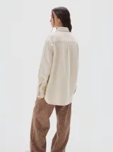 Camisa oversized de jean color crema, con botones rojos en forma de fresa y pespuntes a contratono. Tiene el logo "PASTICHE" bordado en rojo en el pecho.