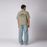 Remera boxy de color crudo con hombro caído y corte cuadrado a la cadera. En el frente presenta un diseño minimalista con texto y un pequeño logo central.