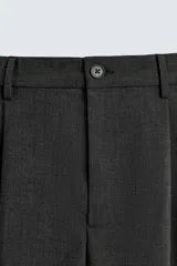 Pantalón negro de corte ancho con pliegues frontales dobles, bolsillos delanteros y traseros de vivo. Cierre frontal con cremallera y botón.