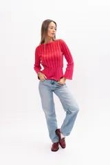 Buzo de punto acanalado con diseño de rayas verticales en tonos fucsia y rojo, de corte ajustado, cuello redondo y mangas largas ligeramente acampanadas.