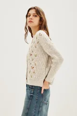 Cardigan de punto color beige con diseño de flores bordadas, escote en V, cierre frontal con botones y mangas largas con puños acanalados.