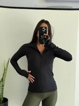 Campera deportiva de ajuste entallado en tejido acanalado color negro, con cierre frontal completo, cuello alto y mangas largas con orificio para el pulgar.