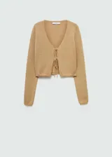 Cardigan de punto color tostado, con cuello en pico, diseño corto y cierre frontal mediante lazos. Posee mangas largas y un tejido de textura ligera.