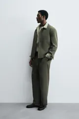 Sobrecamisa de corte boxy fit confeccionada en tejido compacto color beige, con cuello solapa, cierre frontal de botones y bolsillos laterales en costura.