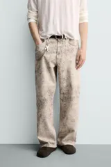 Pantalón de corte baggy fit confeccionado en tejido de algodón con efecto lavado y estampado abstracto en tonos beige y gris. Presenta diseño de cinco bolsillos, cierre frontal con cremallera y botón.