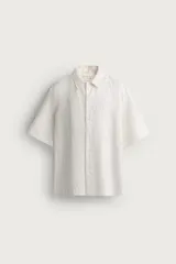 Camisa de lino color blanco, con ajuste relaxed fit, cuello bowling y mangas cortas. Cuenta con cierre frontal de botonadura y aberturas laterales en el bajo.