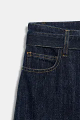 Jeans de tiro alto con pierna ancha, confeccionados en denim azul oscuro. Presentan cinco bolsillos, trabillas en la cintura y un cinturón ajustable del mismo tejido con hebilla metálica. Incluyen pespuntes marcados a tono y cierre frontal con cremallera y botón.