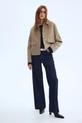 Campera corta de corte recto en color beige melange, con cuello camisero y cierre frontal mediante botones a contraste. Presenta dos bolsillos de parche con solapa en la parte delantera y cuenta con forro interior.