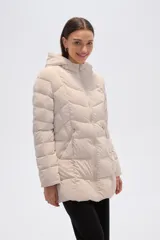 Campera acolchada color beige claro, de largo medio, con capucha y cierre frontal. Presenta costuras horizontales y diagonales que crean un efecto matelassé.