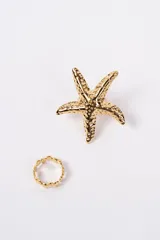 Set de dos anillos en color dorado. Incluye un anillo con diseño de estrella de mar con textura y un anillo fino con diseño de eslabones pequeños.