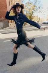 Falda midi negra con efecto piel, diseño cruzado en el delantero y flecos en el bajo. Cierre lateral con cremallera oculta.