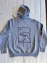 Hoodie gris con capucha y cordón ajustable, corte oversize y estampa en la espalda de una ola dentro de un recuadro.