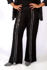 Pantalón negro de corte recto con aberturas laterales en el bajo y detalle de bandas verticales brillantes con strass a lo largo de cada pierna.