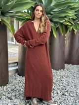 Vestido midi de punto color azul marino, con cuello en V, mangas largas y diseño holgado. Presenta un patrón de rombos en relieve y aberturas laterales con botones decorativos en el ruedo.