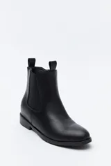 Bota tipo chelsea de caña media confeccionada en cuero sintético, con paneles laterales elásticos y presillas superiores. Presenta un diseño minimalista con suela plana y punta redondeada.