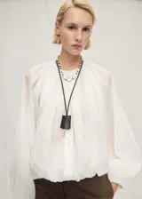 Chaqueta de poliamida blanca, con diseño semitransparente, cuello redondo fruncido, cierre frontal de cremallera, mangas largas con puños elásticos y bajo fruncido.