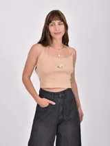 Musculosa color beige claro, de tejido acanalado, con tirantes finos y un pequeño bordado de una sombrilla y una reposera en el pecho.