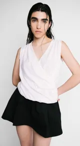 Blusa blanca sin mangas con escote en V cruzado y drapeado.