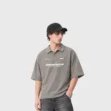 Chomba gris claro de manga corta, con cuello polo, cierre frontal parcial con botones y estampa tipográfica en el pecho.