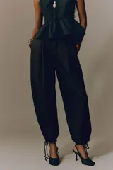 Pantalón tobillero negro de tejido arrugado, con cintura de tiro alto, pliegues delanteros y corte holgado de piernas barrel con elástico y cordón ajustable en los tobillos.