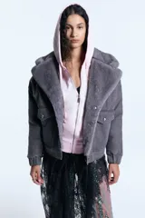 Campera reversible de denim gris con interior de piel ecológica. Presenta cierre frontal con botones metálicos, bolsillos frontales con solapa y puños elásticos. El diseño combina un estilo clásico de jean con la calidez de la piel sintética.