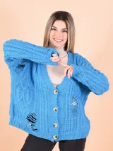 Cárdigan tejido de punto grueso color celeste con diseño trenzado y roturas. Tiene cuello en V, cierre frontal con botones y mangas largas.