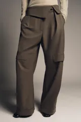 Pantalón de tiro medio color marrón oscuro, estilo cargo, con cintura acabada en vuelta asimétrica, pliegues delanteros y bolsillos laterales y con solapa en las piernas.