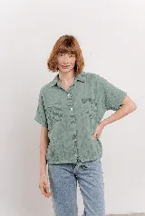 Camisa verde menta de tela arrugada, con cuello clásico, botones frontales, mangas cortas y dos bolsillos delanteros con pespuntes. La base es levemente elastizada y se anuda en el frente.