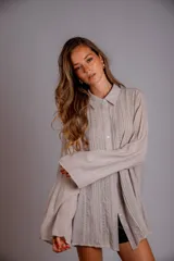 Camisa de manga larga color beige, con cuello camisero y detalles de pliegues verticales y encaje a lo largo del frente. Presenta un calce holgado.