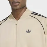 Campera deportiva Adidas Adicolor Classics de corte holgado, color beige con las icónicas tres tiras negras en las mangas y logo del trifolio bordado en el pecho. Cuenta con cierre frontal completo y puños acanalados.