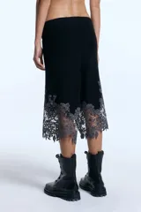 Bermuda de punto en mezcla de lana y alpaca, color negro, de tiro medio y largo hasta la rodilla. Presenta cintura elástica con cordón ajustable y un delicado detalle de encaje gris en el ruedo con diseño irregular.
