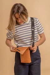 Phonebag pequeña color mostaza, confeccionada en cuero sintético, con solapa frontal y correa ajustable con logo de la marca.